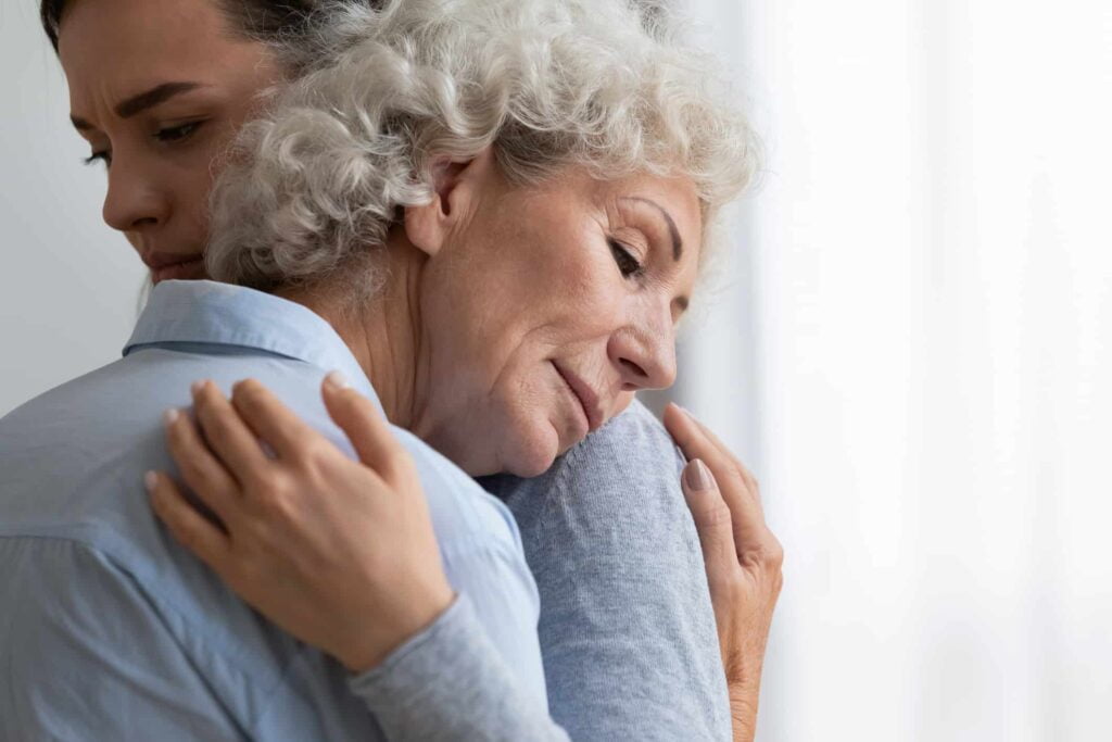 Caring granddaughter comforting, hugging sad grandmother close up